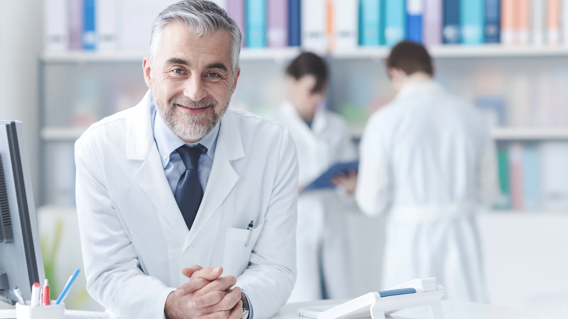 Smiling confident doctor at the reception desk, medical staff working on the background