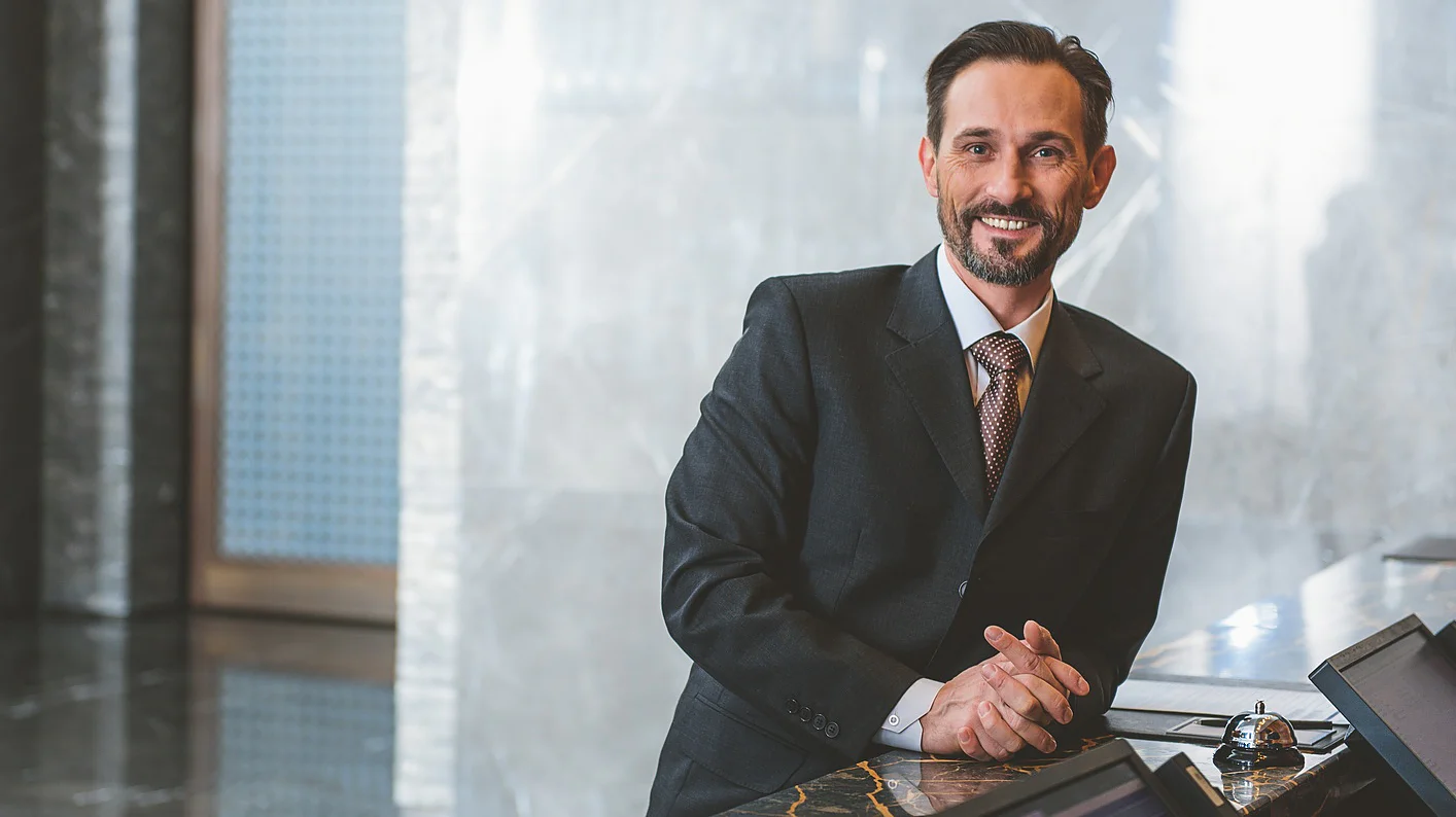 Smiling man in black suit standing near reception desk and looking at camera